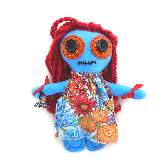 Colorful plush poppet hoodoo doll with red hair, blue body, and floral dress on a white background