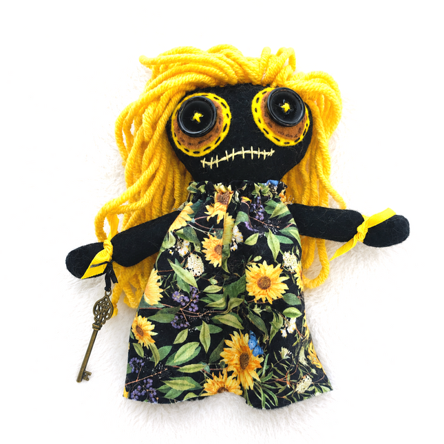 Handmade hoodoo doll with yellow hair and floral dress on a white background