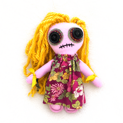 Hoodoo doll with yellow hair and a floral dress on a white background