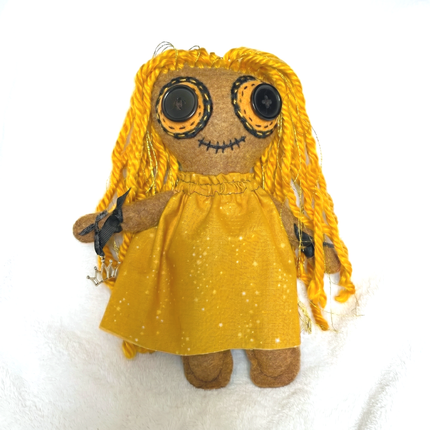 Stuffed hoodoo doll with yellow dress and braided hair on a white background