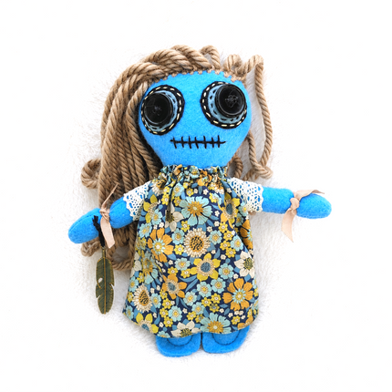 Stuffed Hoodoo doll with blue face, floral dress, and braided hair on a white background