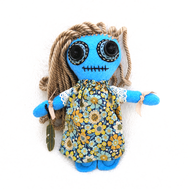 Stuffed Hoodoo doll with blue face, floral dress, and braided hair on a white background