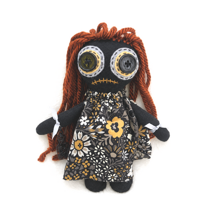 Black hoodoo doll with a floral dress and button eyes on a white background