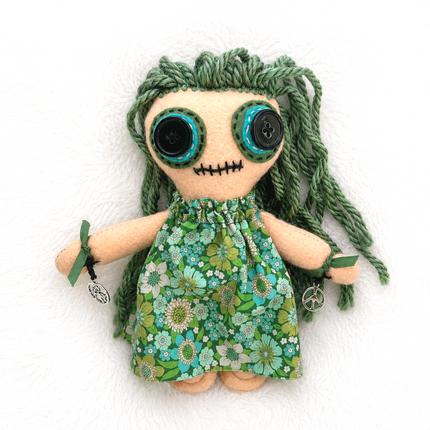 Hoodoo doll with green hair and floral dress on a white background