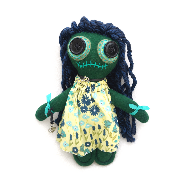 Hoodoo doll with green body, blue hair, and floral dress on a white background