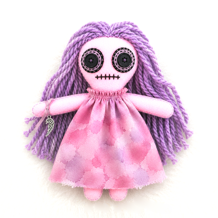 hoodoo protection doll baby with skeleton face and purple braided hair wearing a pink dress on a white background