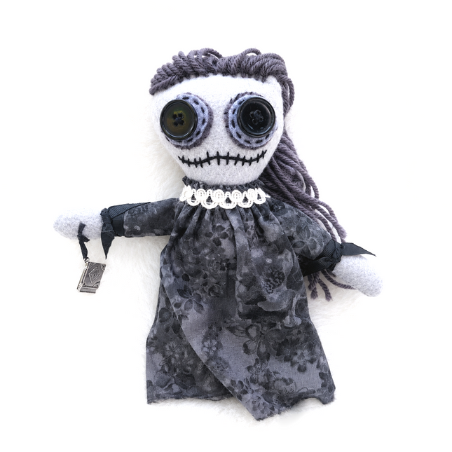 wise woman doll with gray hair and black dress on a white background holding a book of shadows